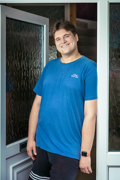 White man in blue tshirt leans against door frame